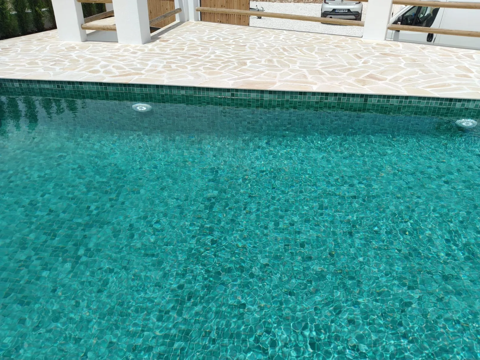 Agua cristalina sobre mosaico verde en una piscina con borde de piedra clara
