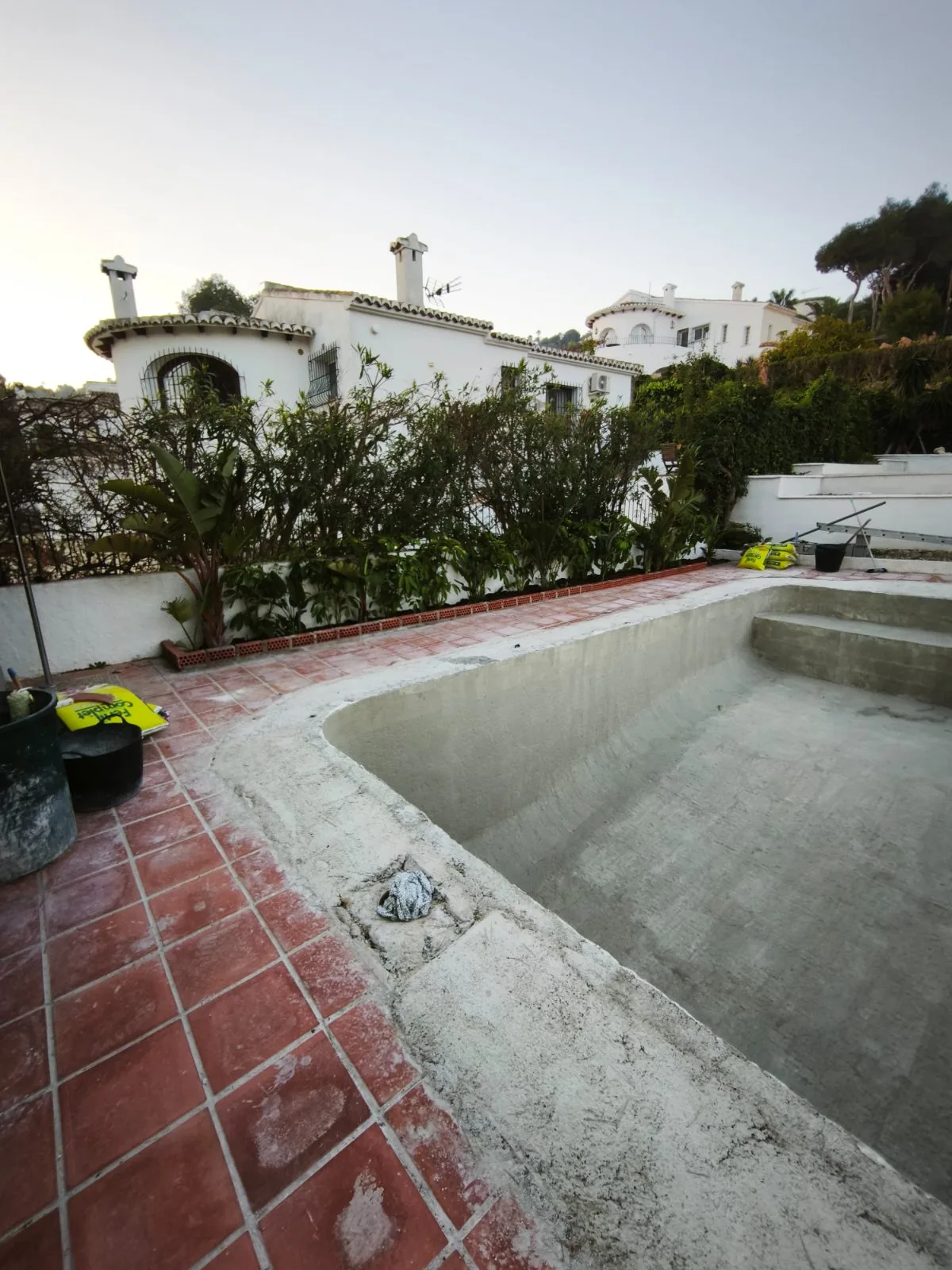 Piscina vacía con el vaso en bruto y borde de baldosa roja antigua junto a una villa