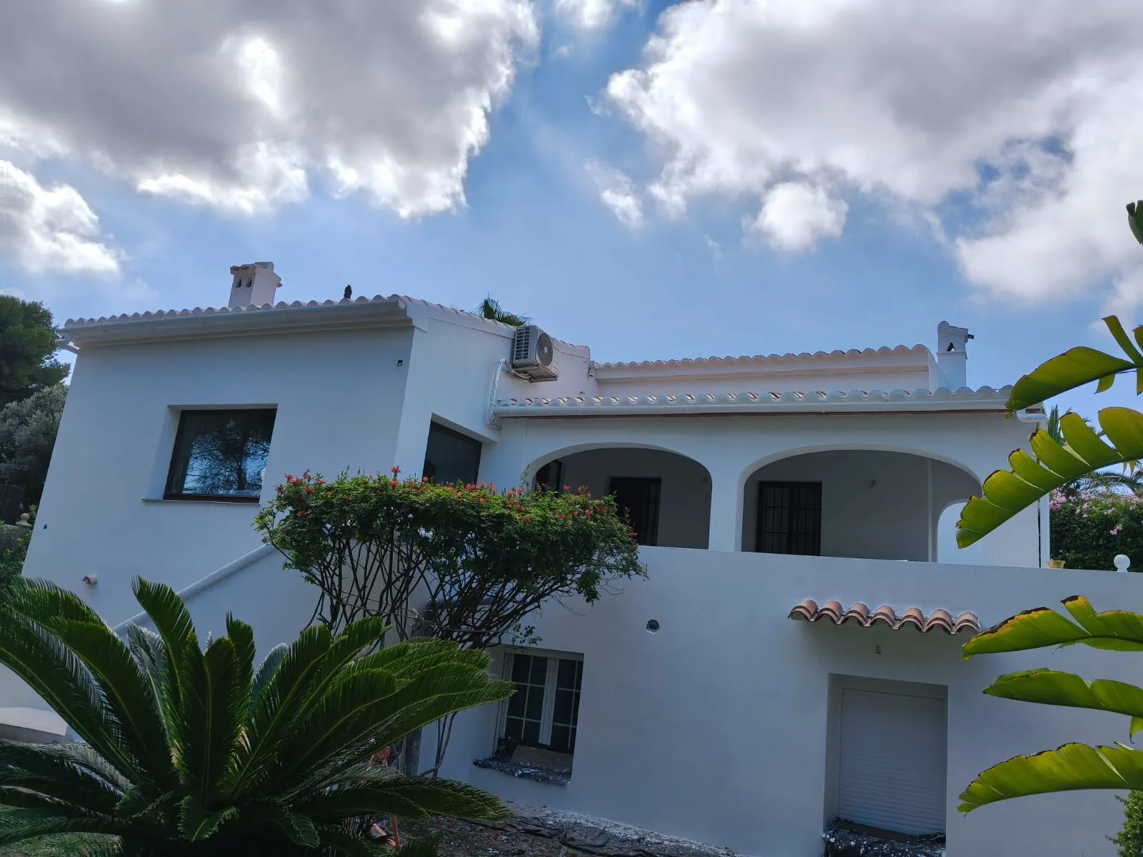Villa con fachada blanca renovada vista desde el jardín bajo cielo azul