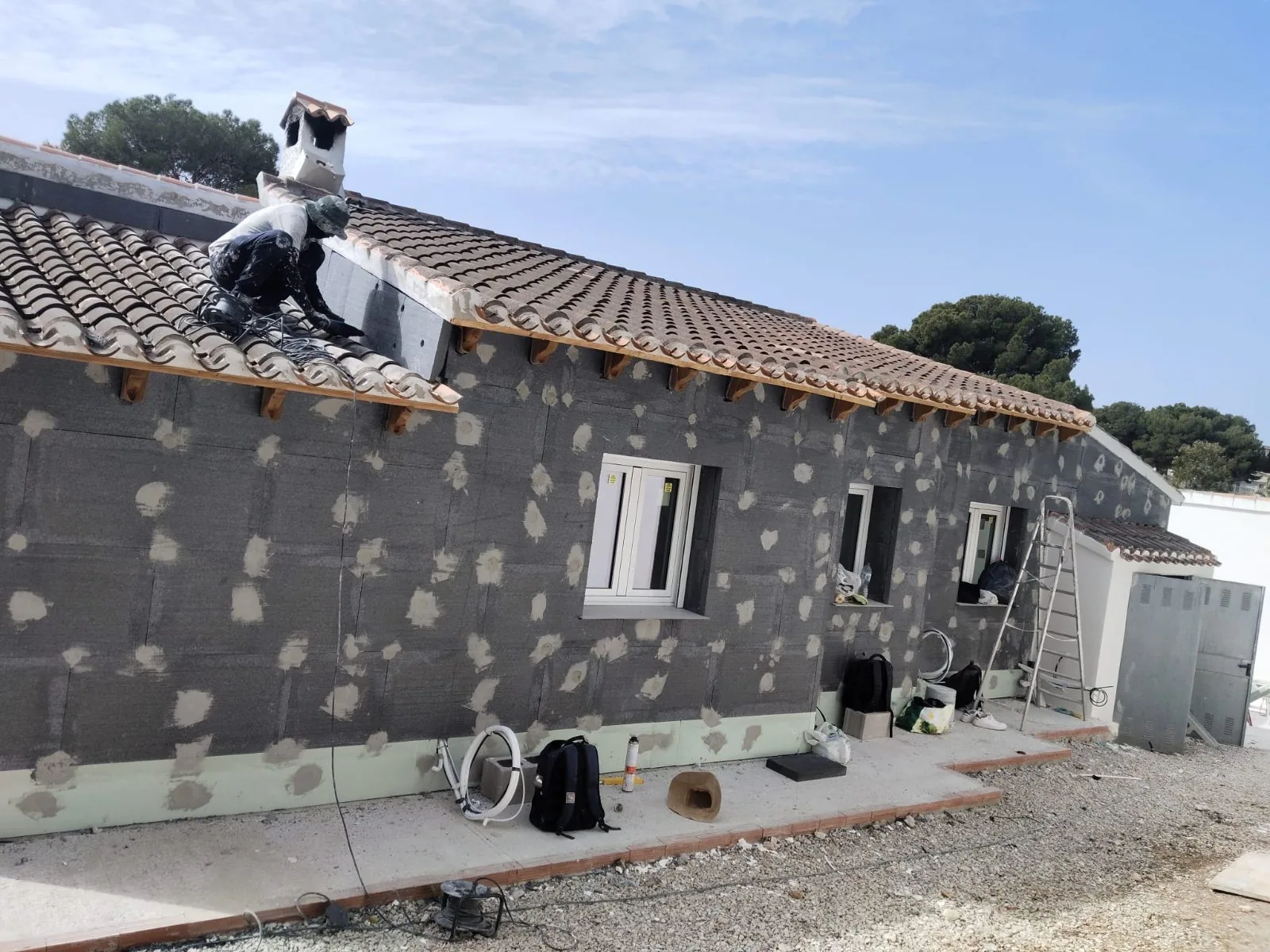 Casa de una planta con paneles aislantes grises fijados en fachada y operario trabajando en el tejado