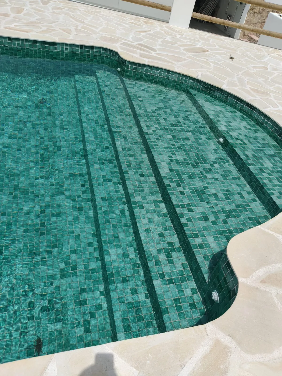 Escalera de piscina con mosaico verde y borde curvo de piedra