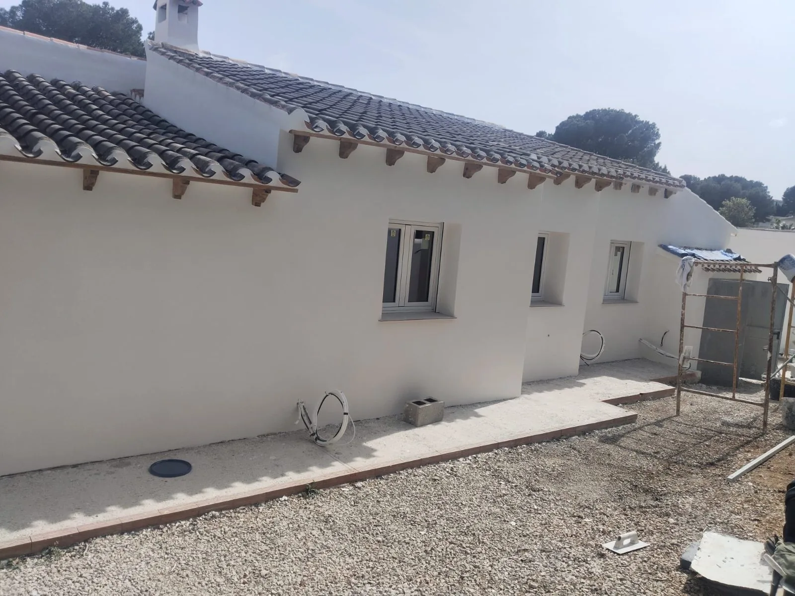 Fachada de vivienda de una planta con revestimiento blanco terminado y tejado de teja