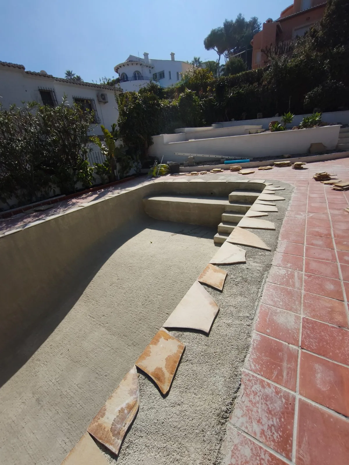 Piscina vacía con escalera y piezas de piedra colocándose en el borde