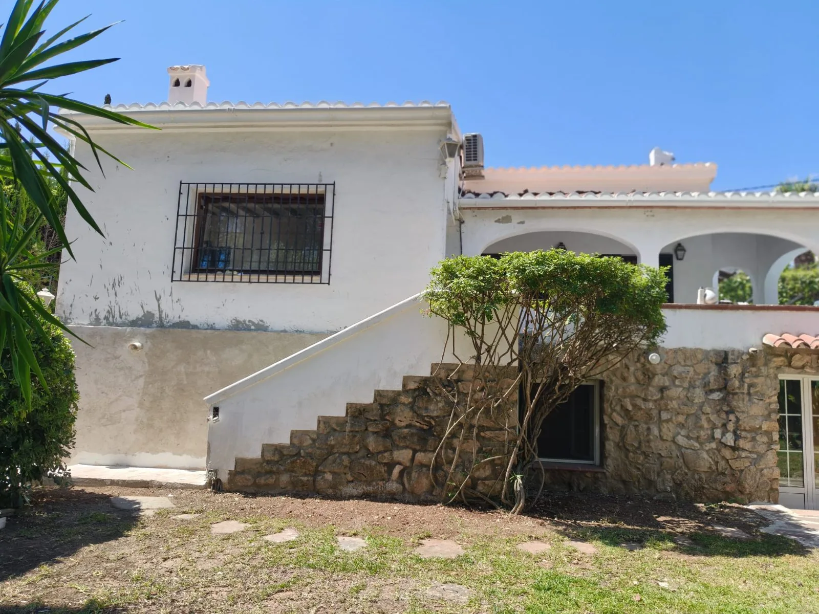 Vivienda con fachada envejecida, escalera exterior y muro de piedra