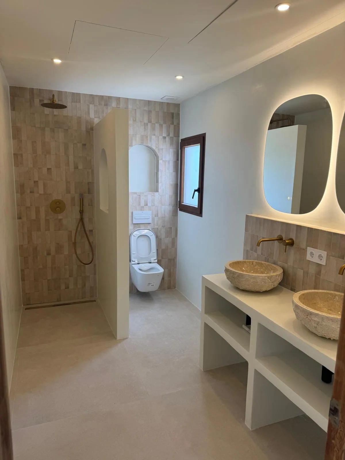 Baño reformado con ducha de obra, lavabos de piedra sobre encimera y espejos con luz