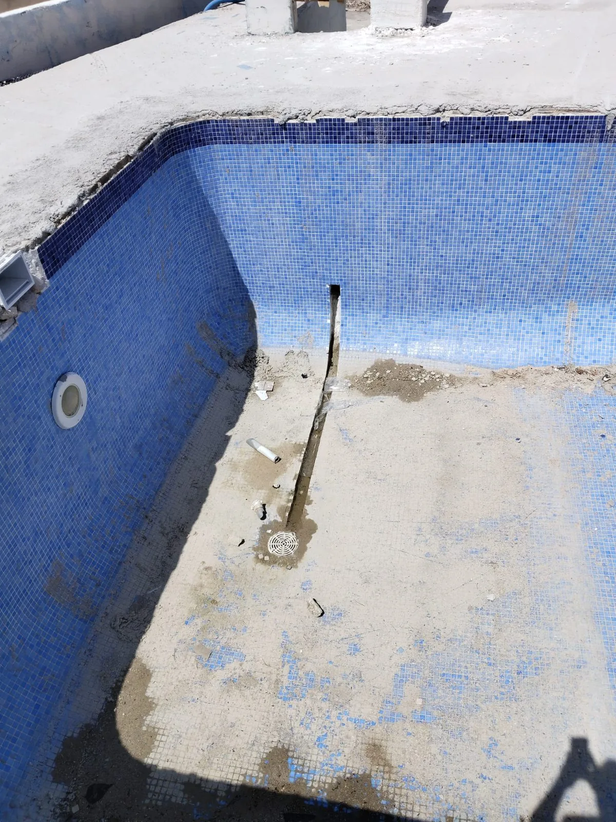 Piscina vacía con mosaico azul desgastado y restos de material en el fondo
