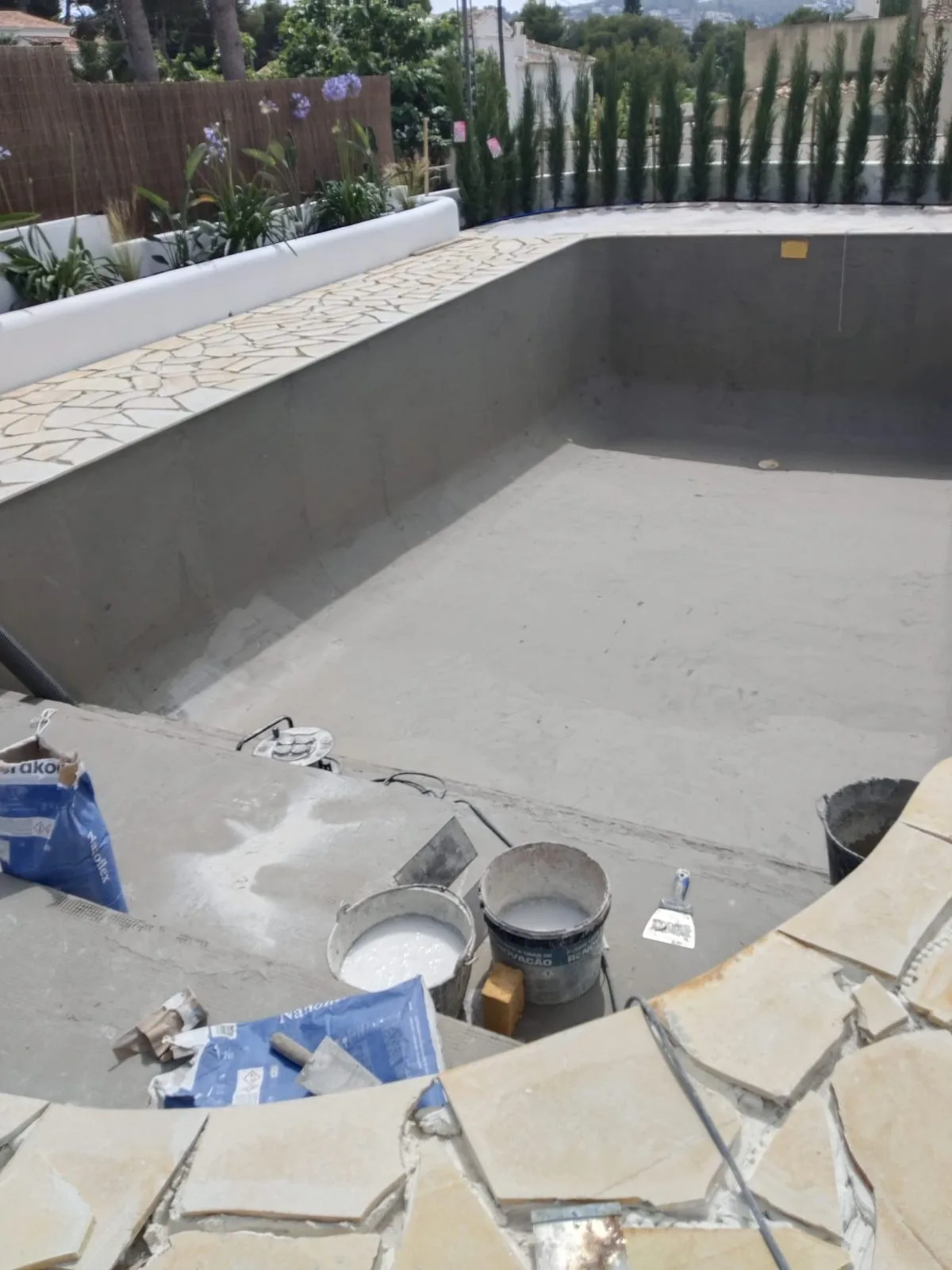 Vaso de piscina con revestimiento gris en obra, cubos de material y borde de piedra en colocación