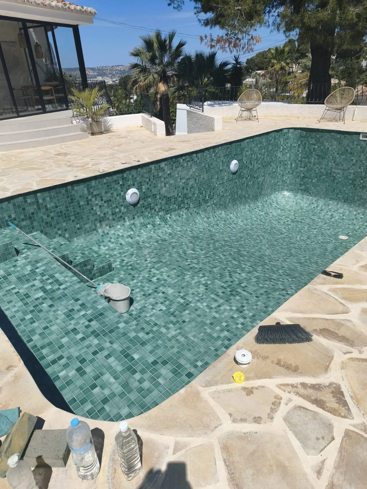 Piscina con mosaico verde y borde de piedra natural, con herramientas aún en el bordillo