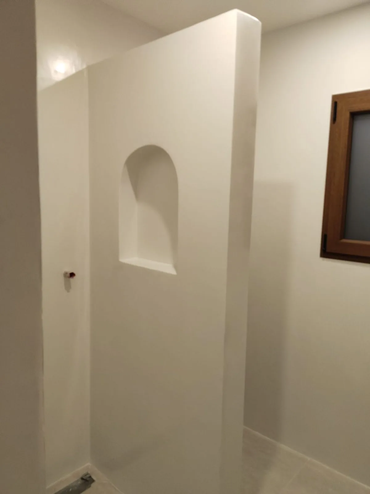 Mampara de obra blanca con hornacina en arco en un baño reformado