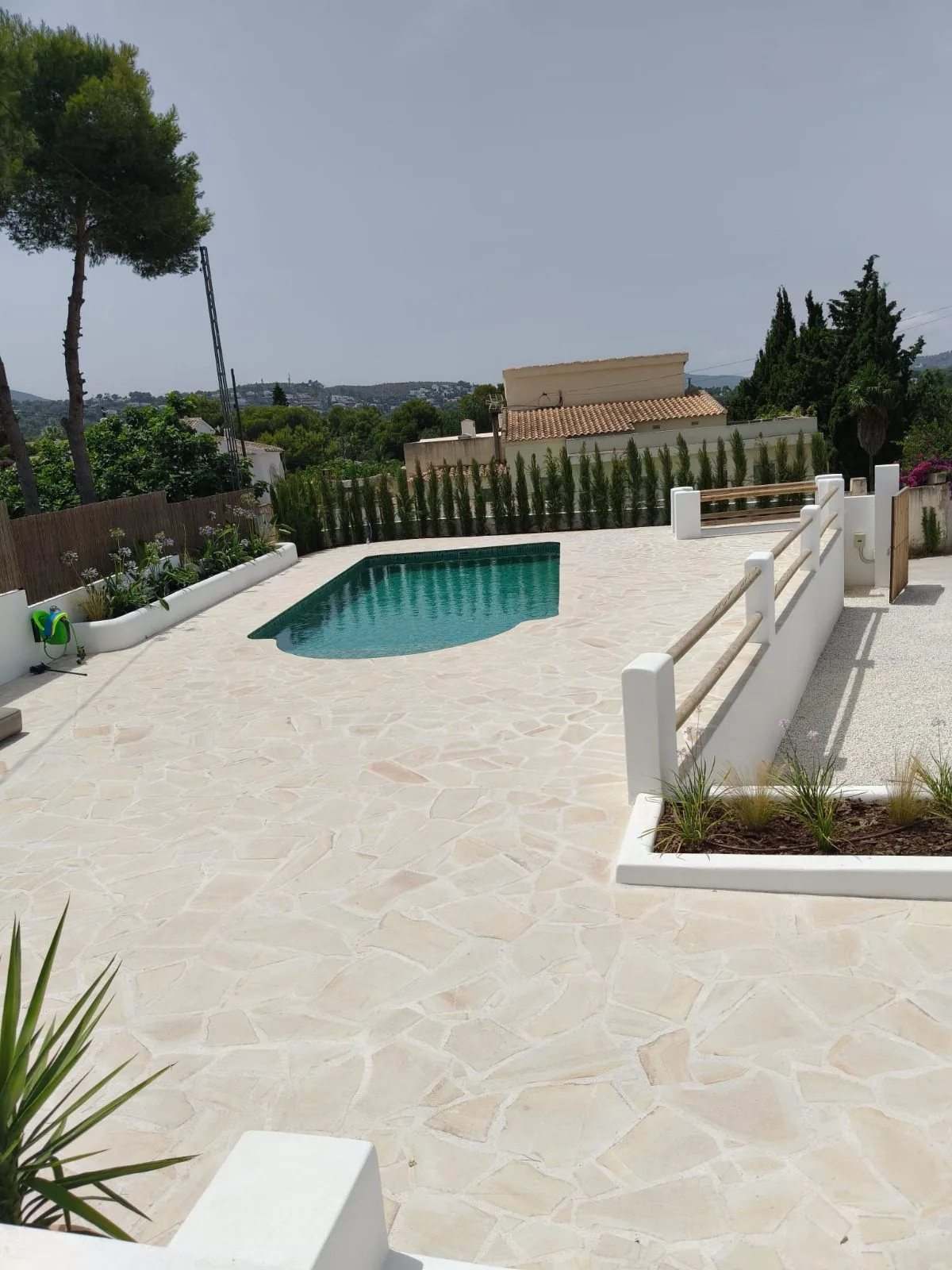 Terraza amplia de piedra natural con piscina al fondo y barandilla blanca